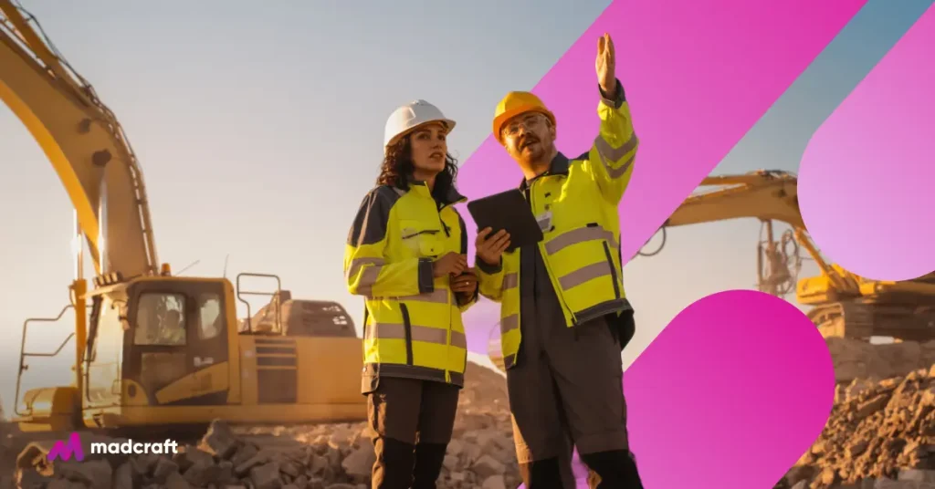 Two construction professionals in high-visibility jackets and hard hats discussing plans on a work site with excavators in the background